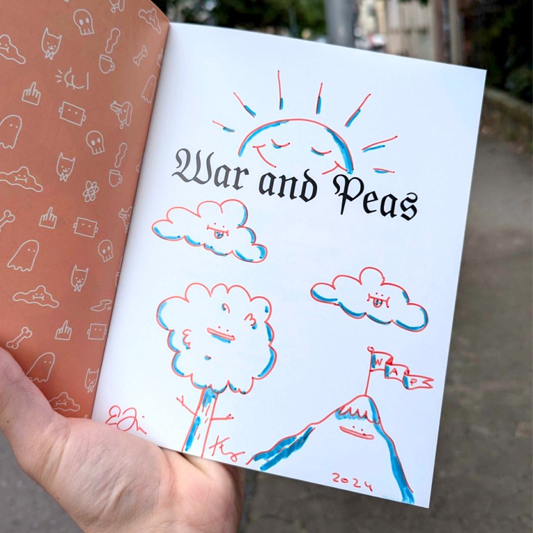 Photo of a signed first page of the book 'Funny Comics for Dirty Lovers' by War and Peas. The page features an original drawing of different nature characters along with the title 'War and Peas' and signatures by the artists. The background shows whimsical patterns with various doodles including ghosts, cats, and bones, creating a playful aesthetic.