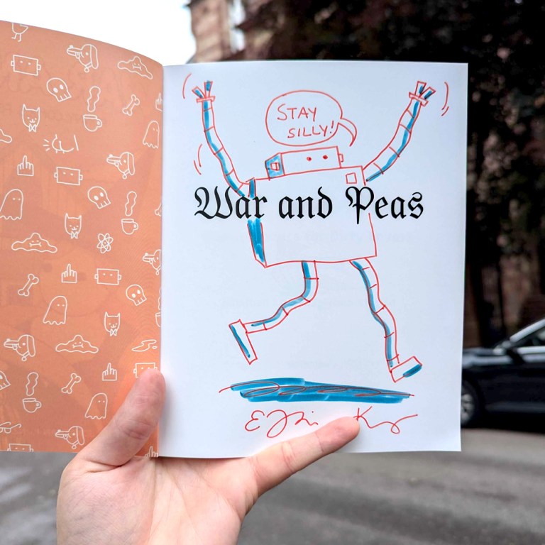 Photo of a signed first page of the book 'Funny Comics for Dirty Lovers' by War and Peas. The page features an original drawing of a cheerful robot saying 'Stay Silly!' along with the title 'War and Peas' and signatures by the artists. The background shows whimsical patterns with various doodles including ghosts, cats, and bones, creating a playful aesthetic.