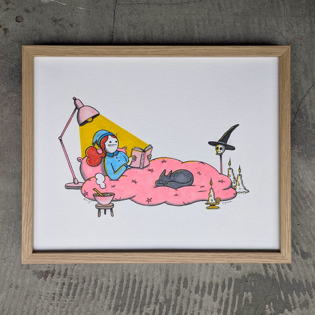 Hand-drawn original art of a witch character lounging on a pink blanket with a black cat, engrossed in the book ‘Coven in the Woods’ under a warm lamp. Framed in German-crafted premium wood, it’s a perfect gift for lovers of whimsical, artistic home decor and unique witchy aesthetics.